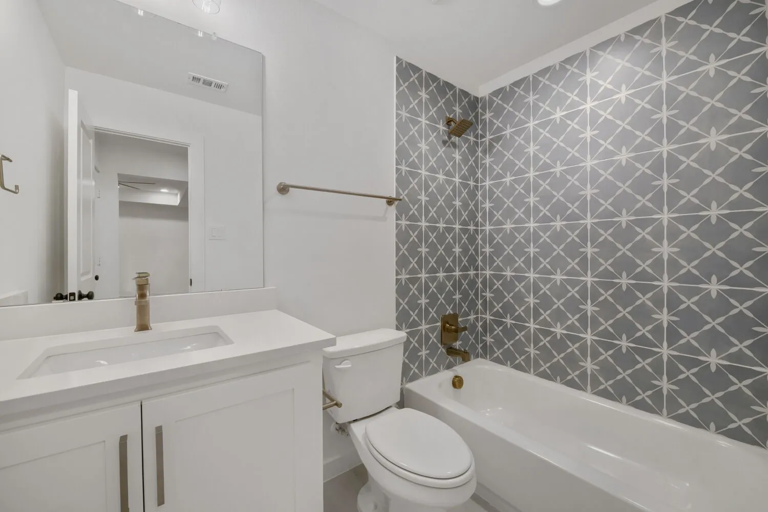 Bathroom featuring patterned wall tile, a white vanity with an integrated sink, a full-width mirror, and brass-finish fixtures