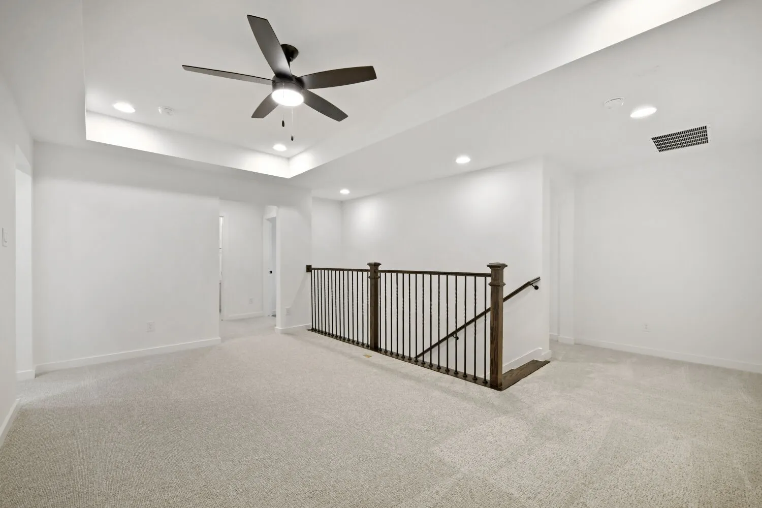 Carpeted upper-level space featuring a tray ceiling with recessed lighting and a ceiling fan