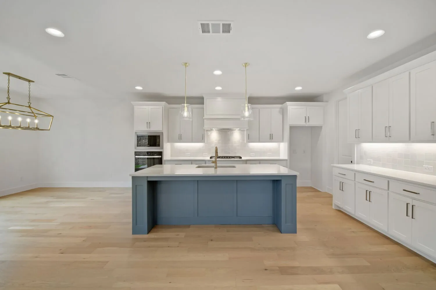 Kitchen featuring a blue island with a light-toned countertop, recessed lighting, wood-finish flooring, white cabinetry, and stainless steel built-in appliances