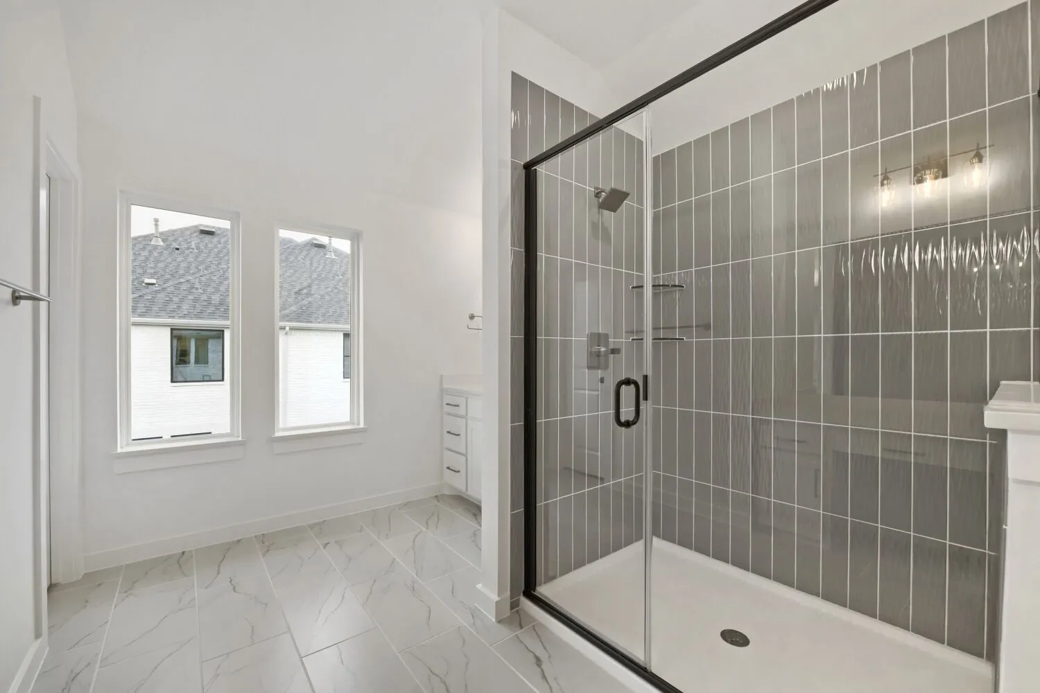 Spacious bathroom featuring a frameless glass shower enclosure with matte black accents, vertical gray subway tile, and a built-in shower bench