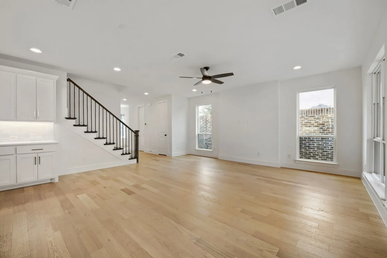 Bright open-concept living space with light wood-finish flooring, recessed lighting, and a modern ceiling fan