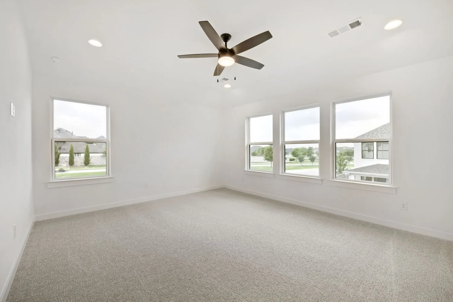Spacious room featuring light-colored carpeting, multiple windows providing ample natural light, a ceiling fan with integrated lighting, and recessed ceiling lights