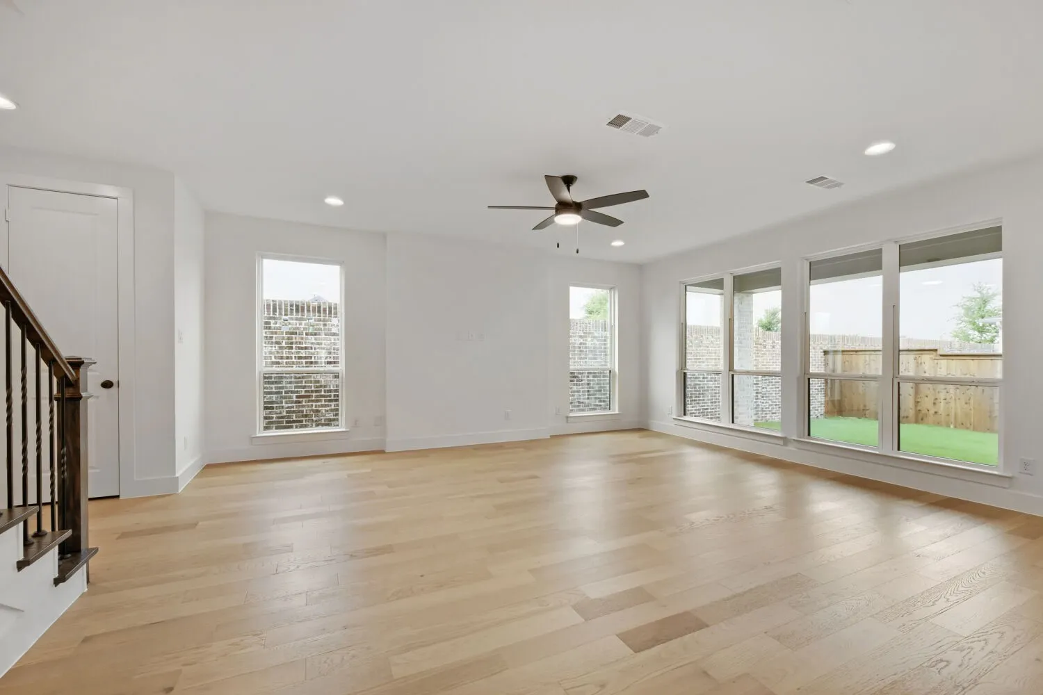 Spacious interior with light wood-finish flooring, recessed lighting, and a dark-toned ceiling fan