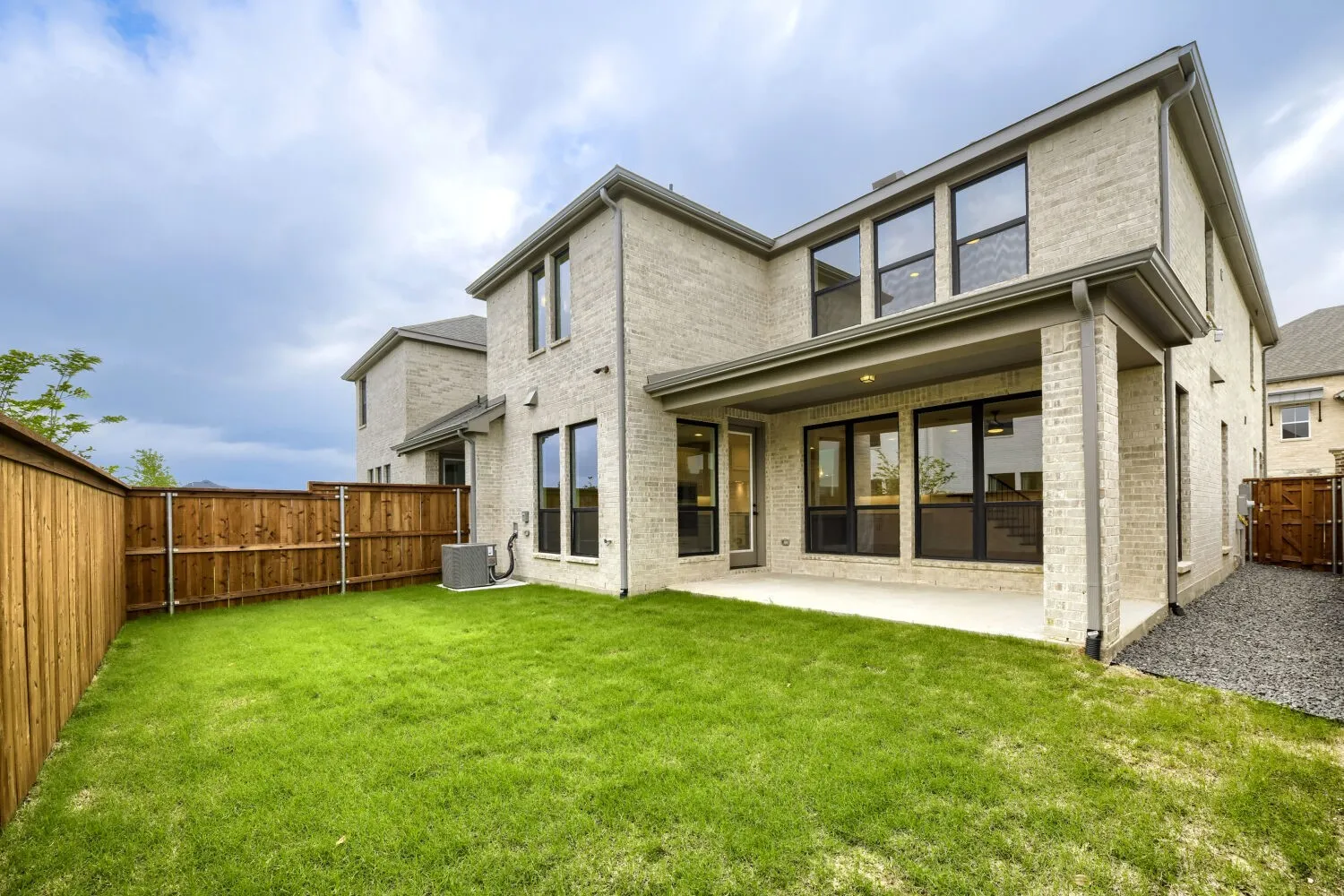 Expansive fenced backyard featuring a covered patio, manicured lawn, and multi-pane windows