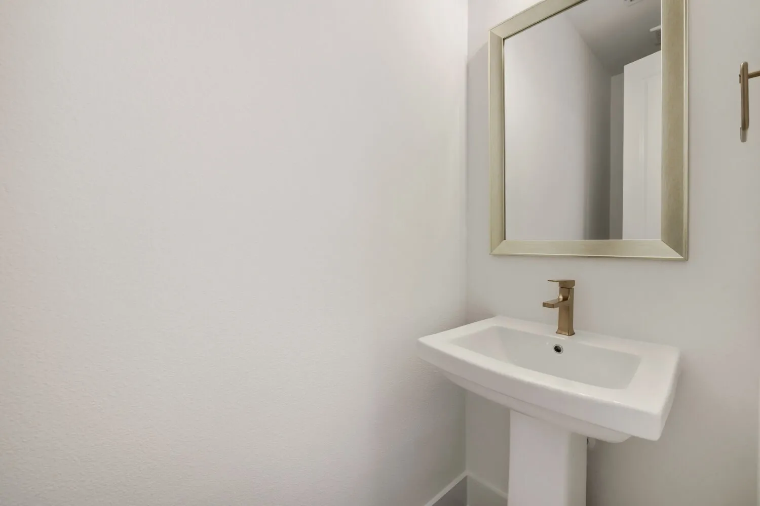 Pedestal sink with a gold-tone faucet, complemented by a framed mirror and a gold-tone towel bar