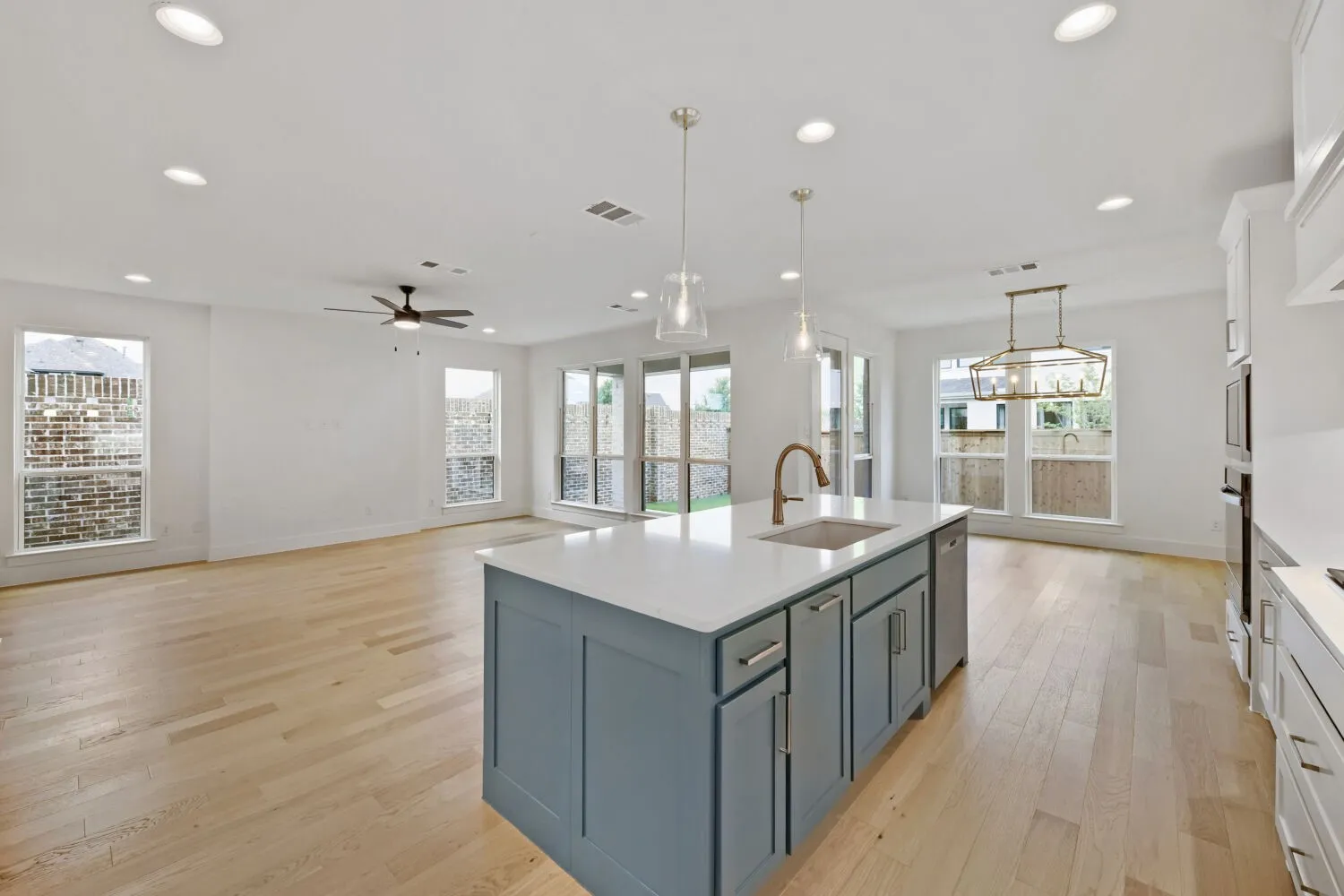 Kitchen island with a light countertop and integrated sink, pendant lighting, hardwood flooring, recessed ceiling lighting, and multiple windows