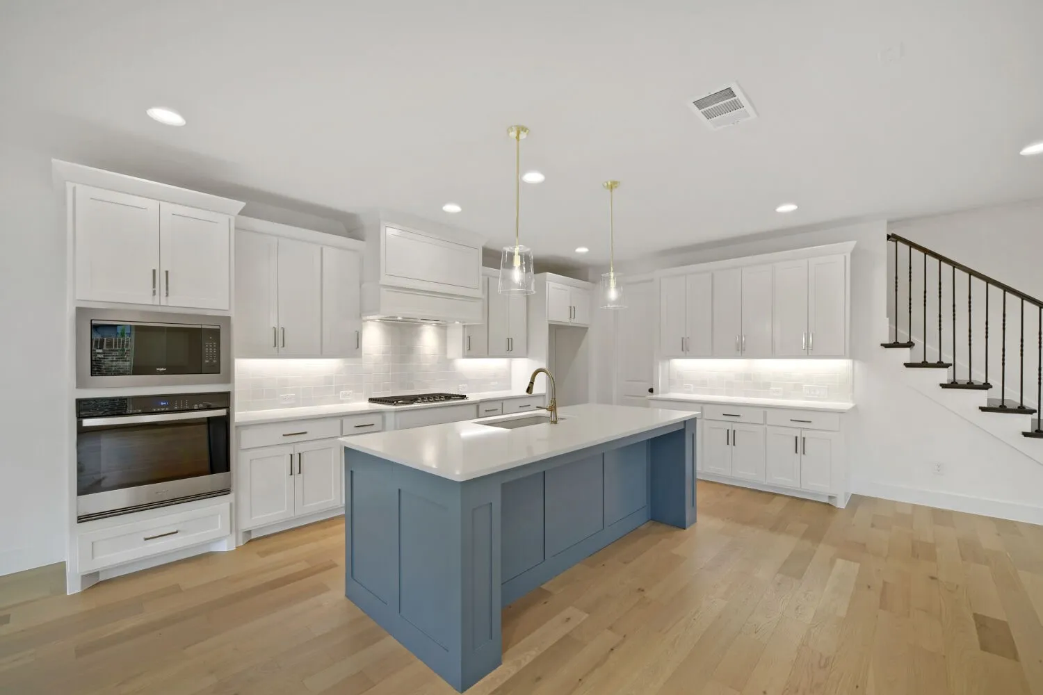 Modern kitchen featuring white shaker cabinetry, stainless steel appliances, a blue island with a white countertop, and hardwood flooring