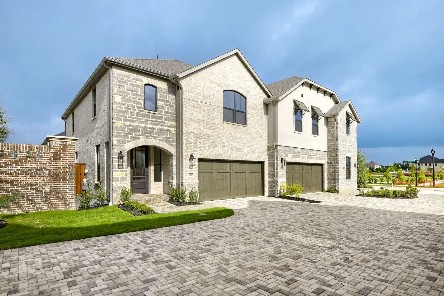 Stone and stucco exterior featuring multiple gables, arched entry, and dark wood-finish garage doors