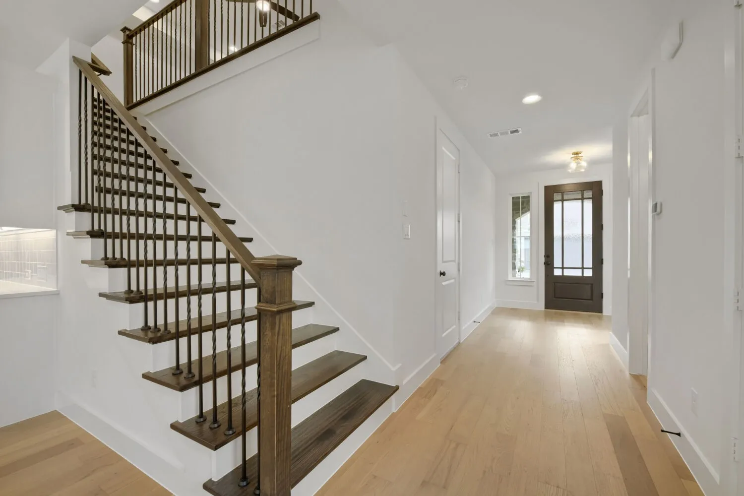 Entry foyer featuring light wood-finish flooring, a dark wood-paneled front door with multiple glass lites, a complementing staircase with dark wood treads and wrought iron balusters, and recessed ceiling lighting