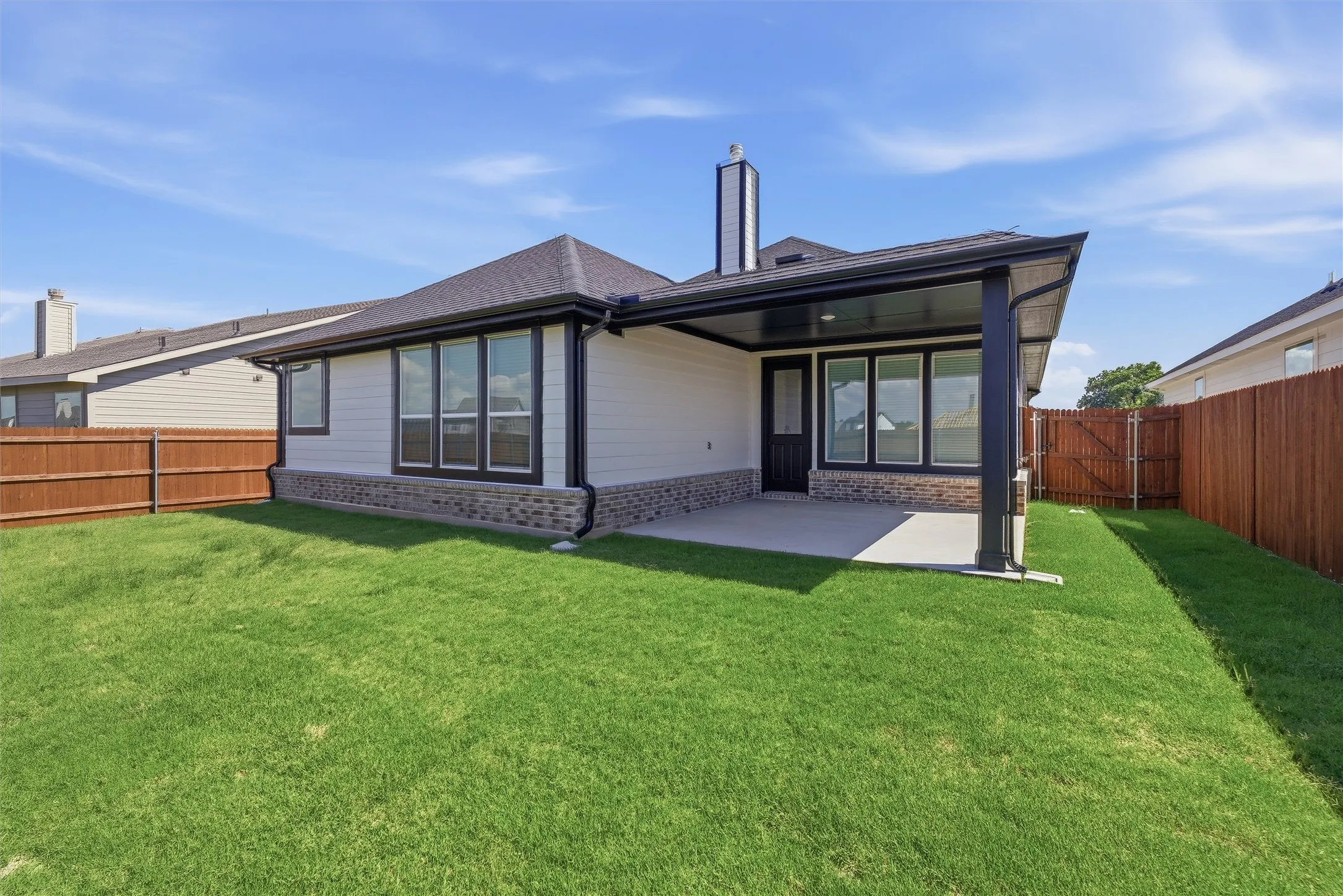 Expansive backyard featuring a covered patio with concrete flooring, white siding, stone veneer accents, and a dark shingle roof