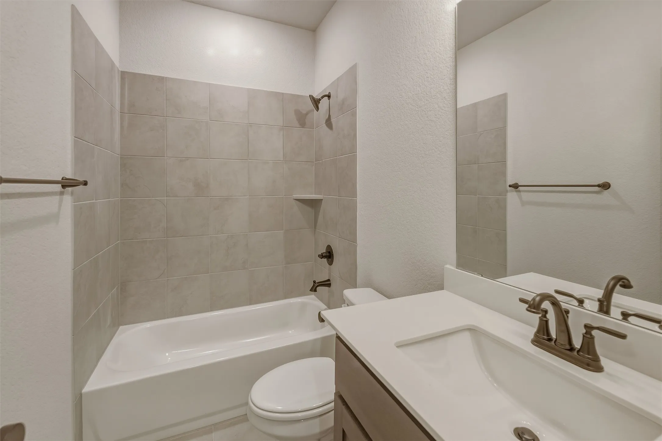 Bathroom featuring a white tub, light-toned tile surround, bronze-finish fixtures, and a vanity with an integrated sink and white countertop