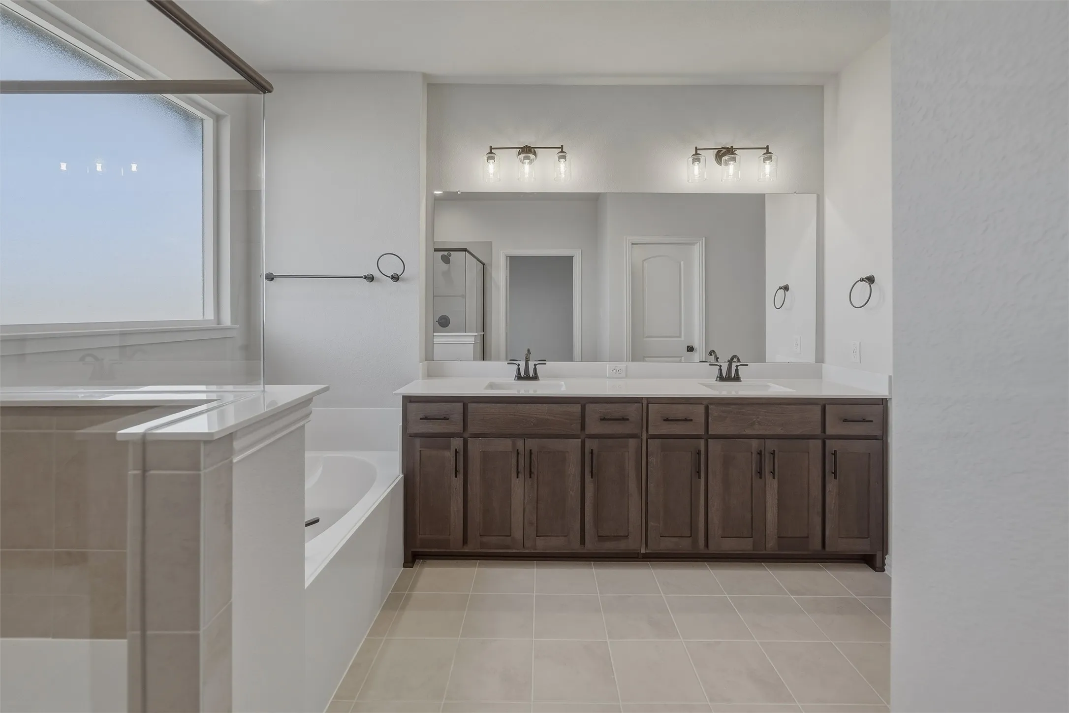 Bathroom featuring a dual vanity with dark wood-finish cabinetry and light countertops, a large framed mirror, and a built-in soaking tub