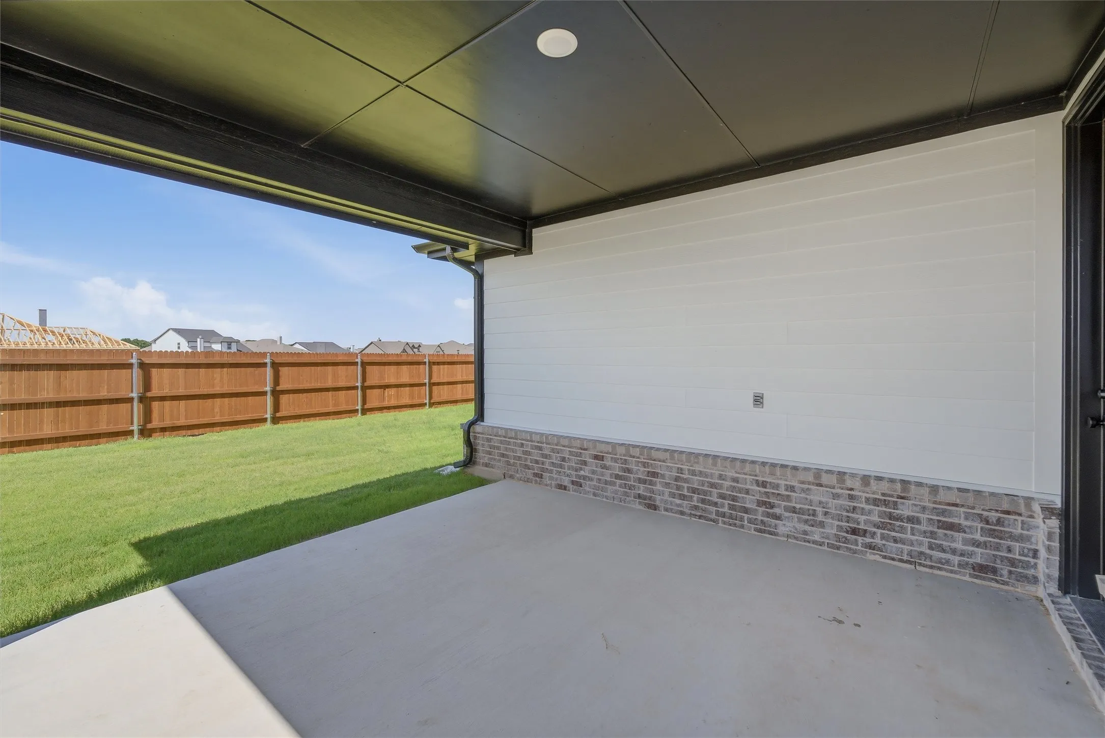 Covered concrete patio with a dark soffit ceiling and white siding