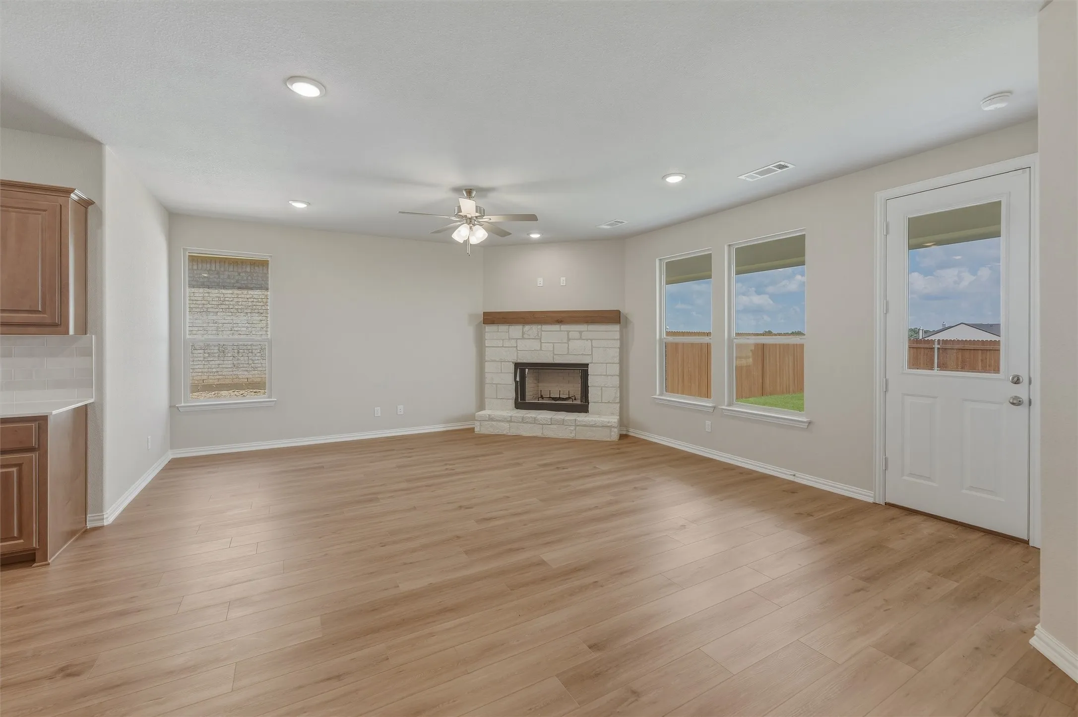 Spacious living area featuring wood-finish flooring, a corner stone fireplace with a wood mantle, recessed lighting, and a ceiling fan