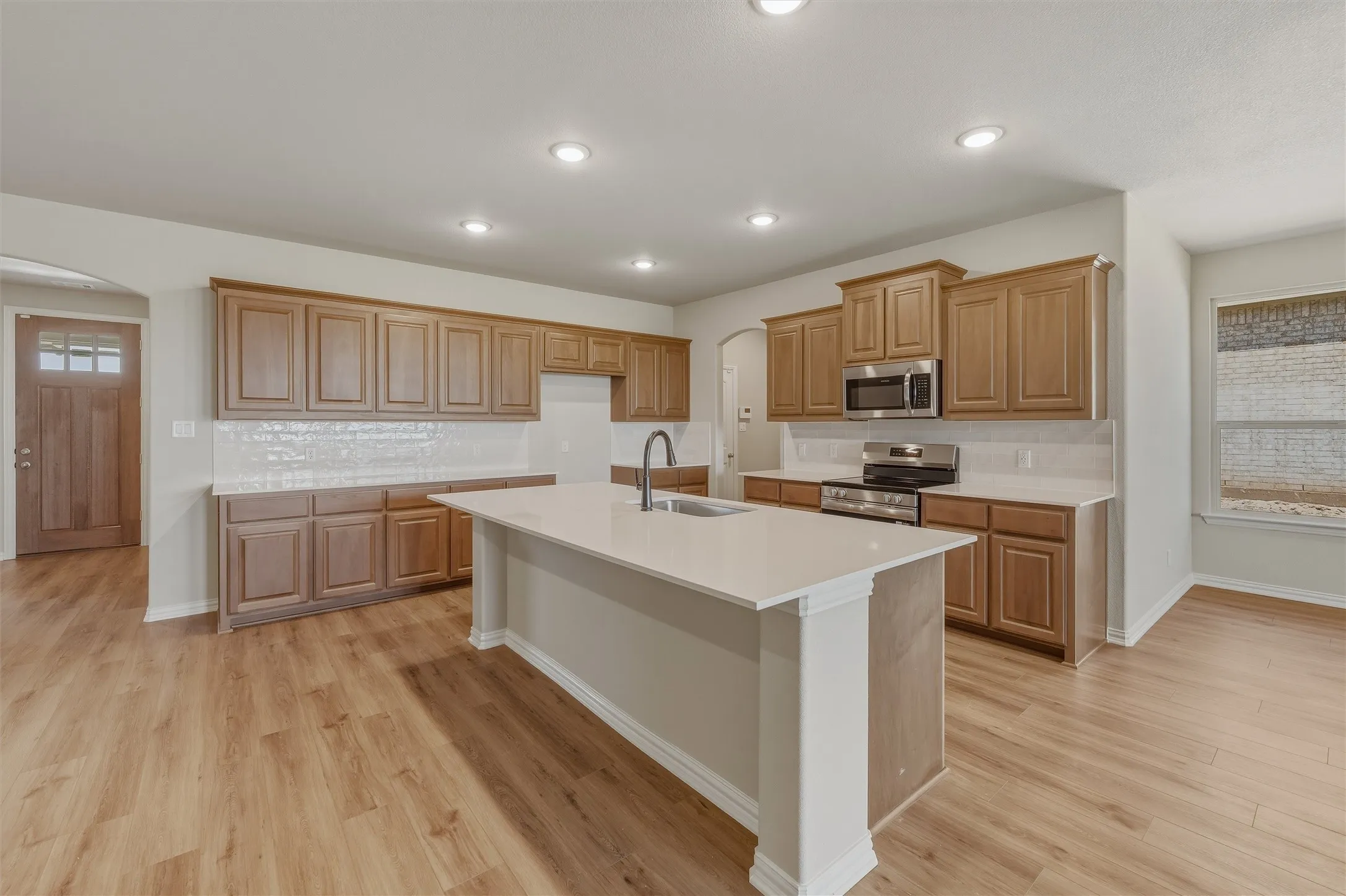 Open-concept kitchen featuring an expansive center island with an integrated sink, wood-finish flooring, and recessed lighting