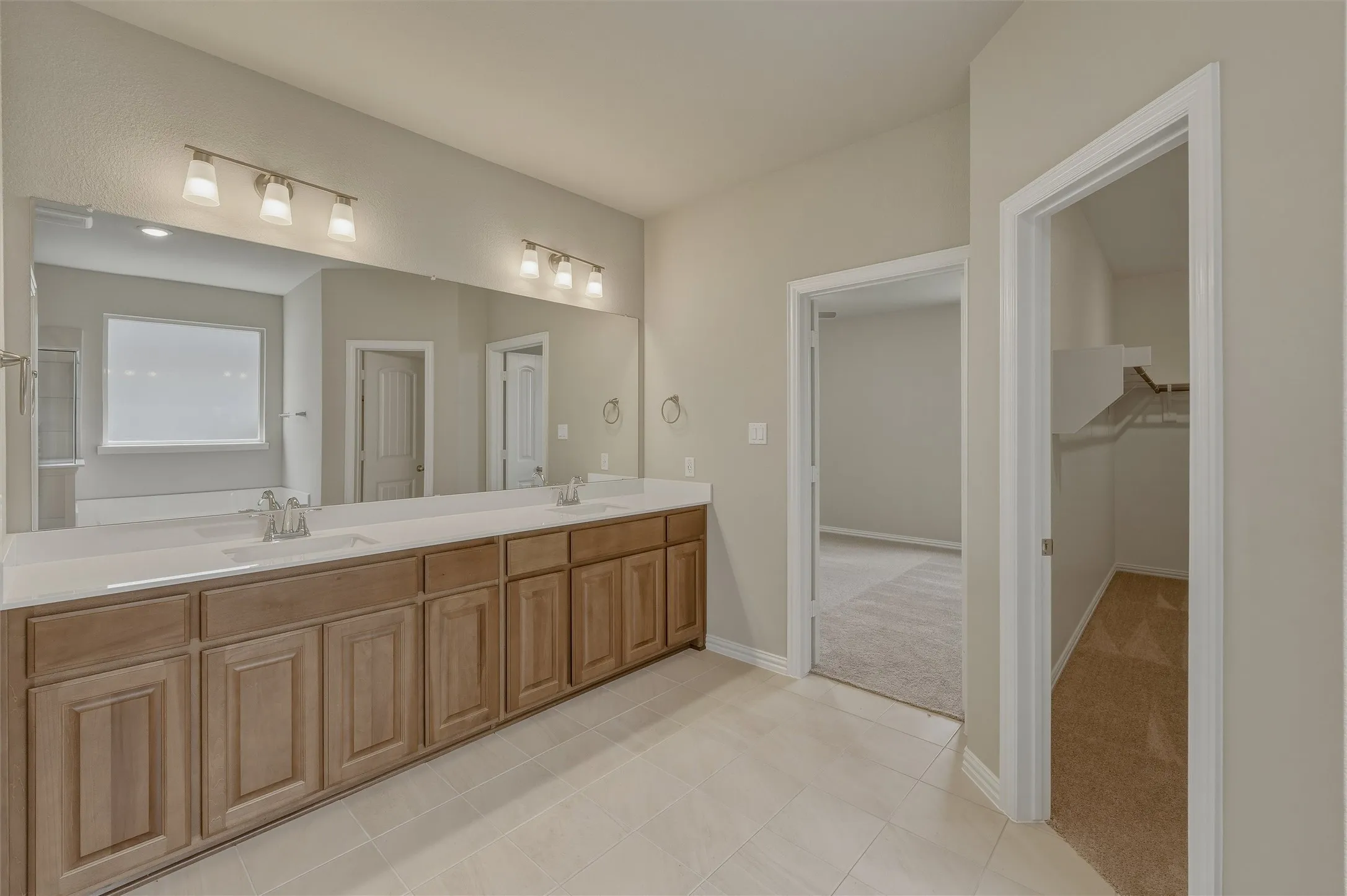 Double vanity with light wood-finish cabinetry, white countertops, and dual undermount sinks