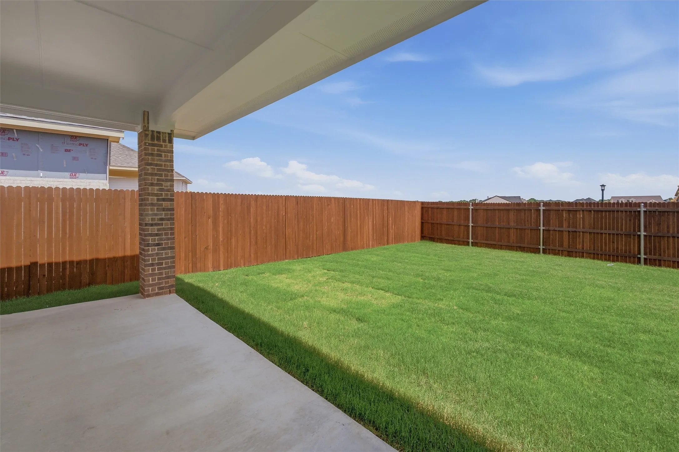 Expansive backyard featuring a covered concrete patio, lush green lawn, and a privacy fence