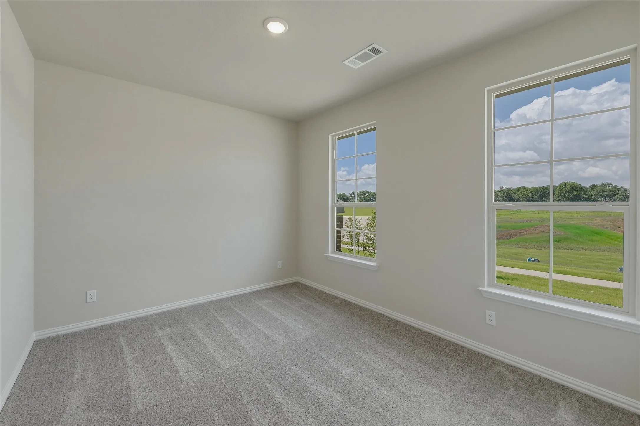 Bright room featuring two large windows, neutral gray carpet, white baseboards, and a recessed ceiling light