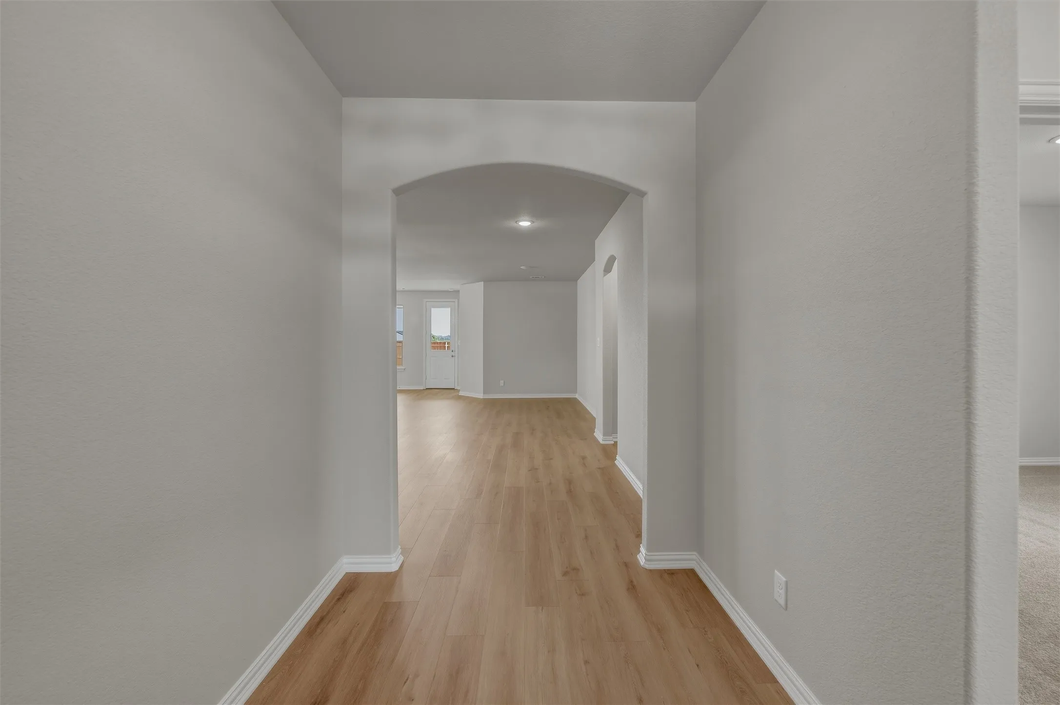 Archway entry to a main living area featuring light wood-finish flooring and light gray painted walls