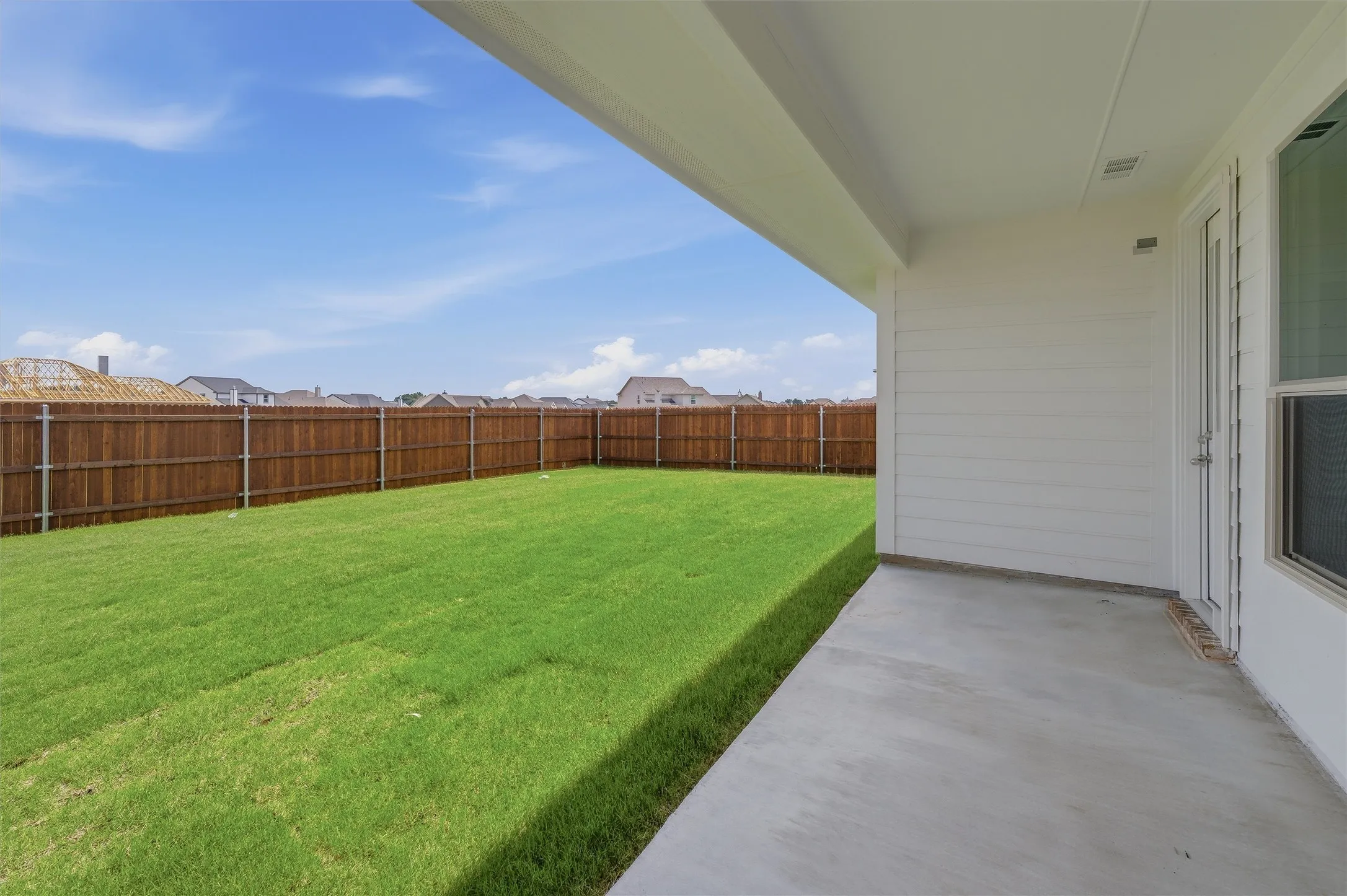 Expansive backyard featuring a manicured lawn, full privacy fencing, and a concrete patio