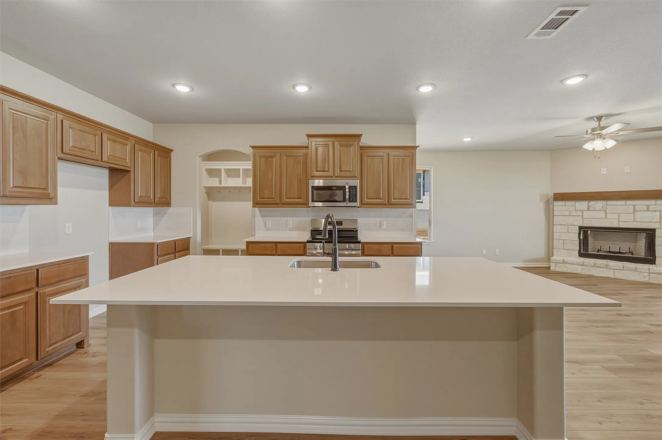 Kitchen island with an undermount sink, quartz countertop, wood-finish cabinetry, stainless steel appliances, and wood-finish flooring