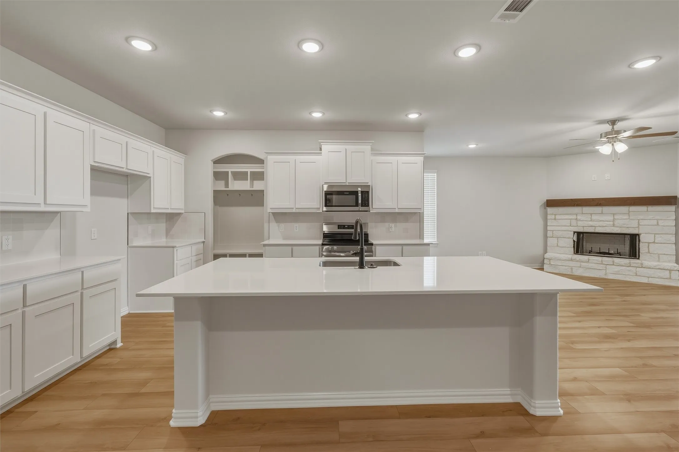 Open-concept kitchen featuring an expansive island with an undermount sink, white cabinetry, stainless steel appliances, and wood-finish flooring