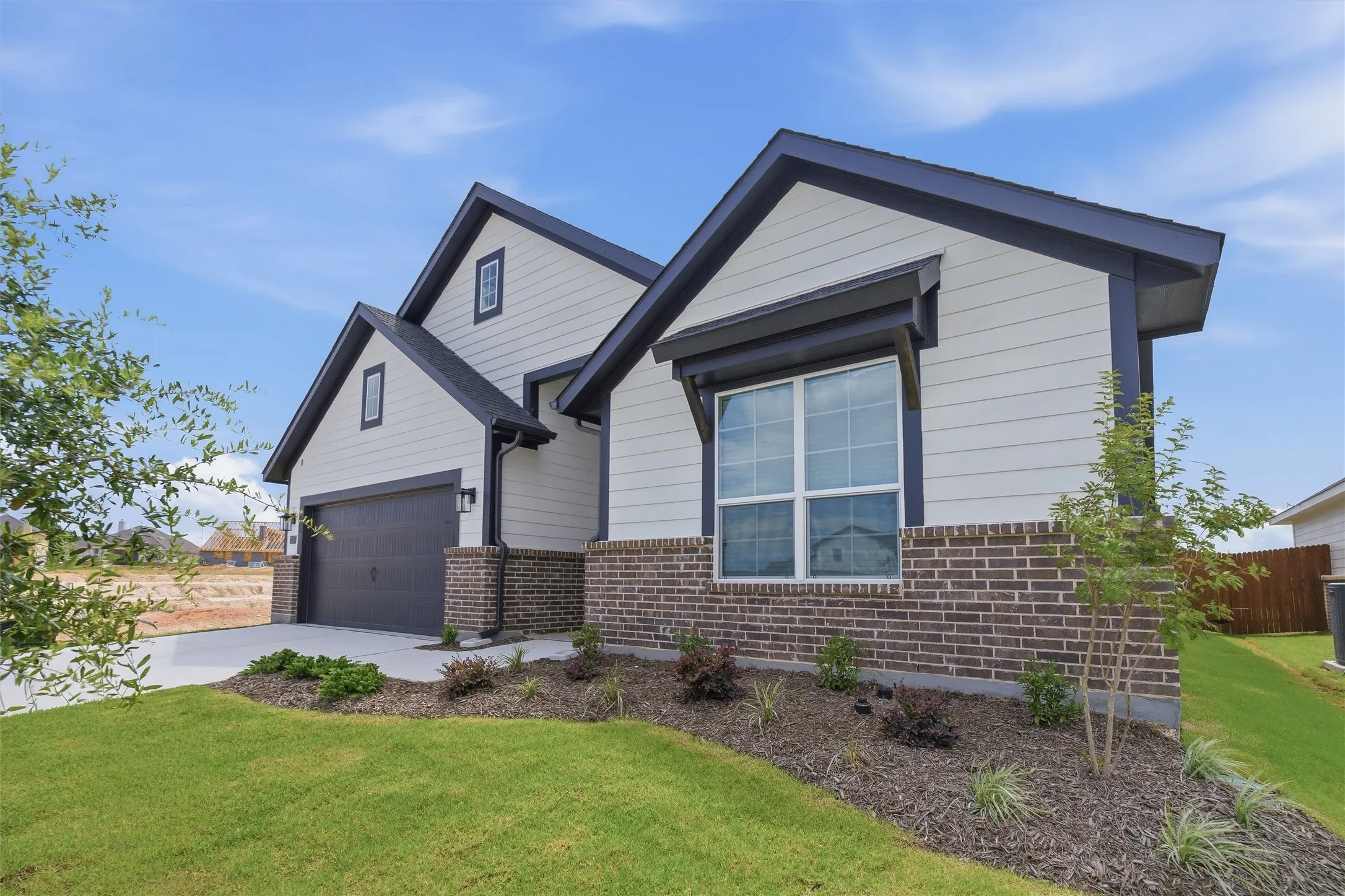 Modern home exterior featuring light horizontal siding, dark trim, a dark gray garage door, and a brick facade