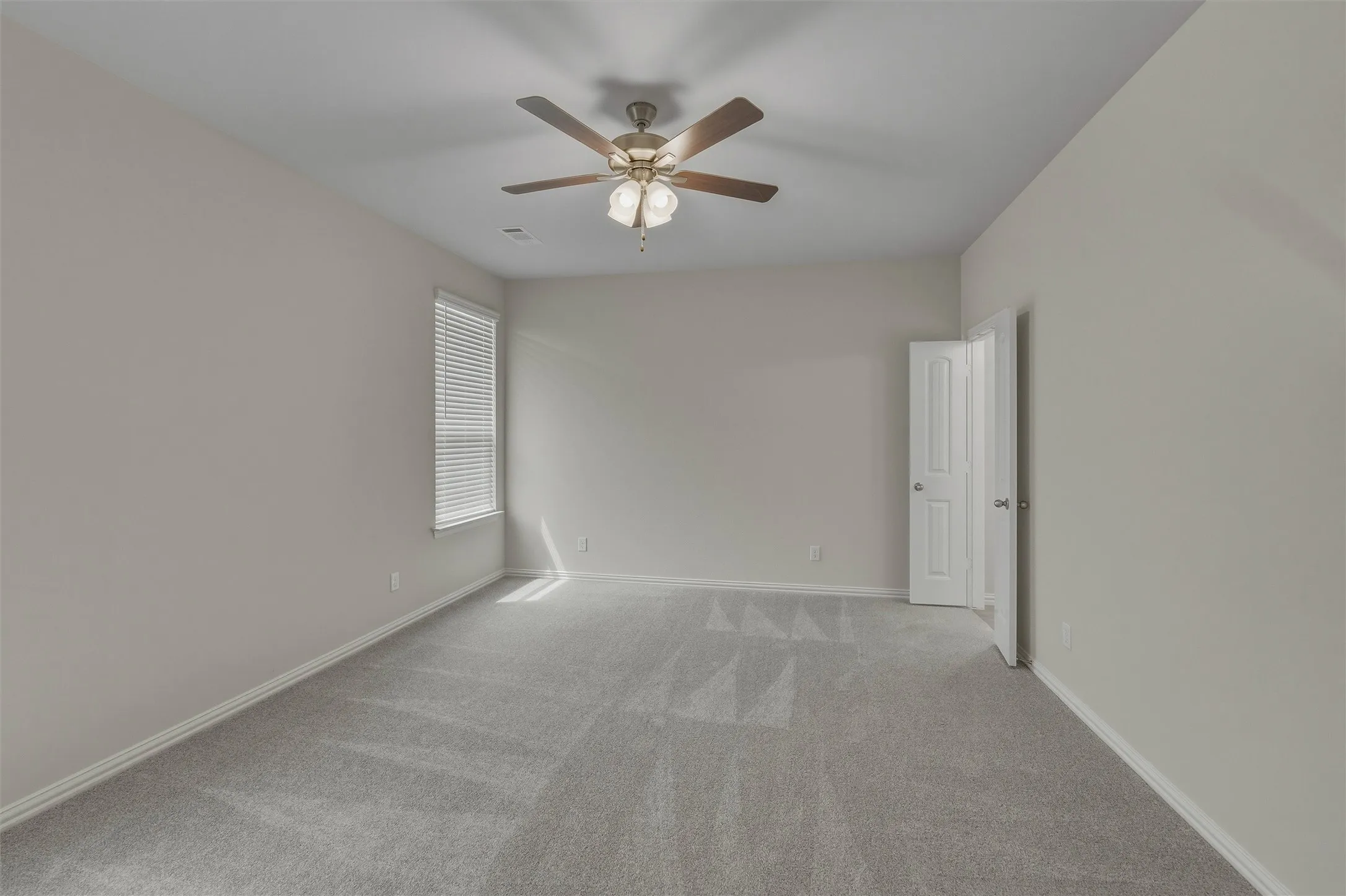 Spacious room featuring neutral carpeting, light-toned walls, and a ceiling fan with integrated lighting