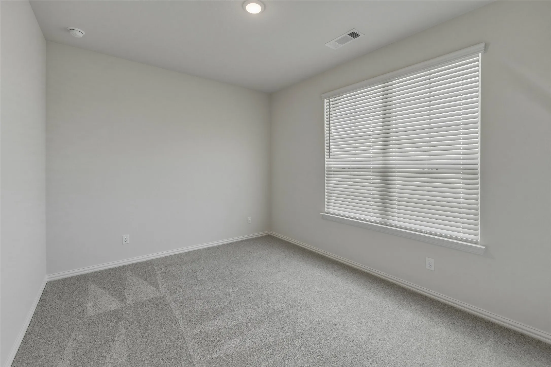 Spacious room featuring neutral paint, gray patterned carpet, a large window with blinds, recessed lighting, and white baseboards
