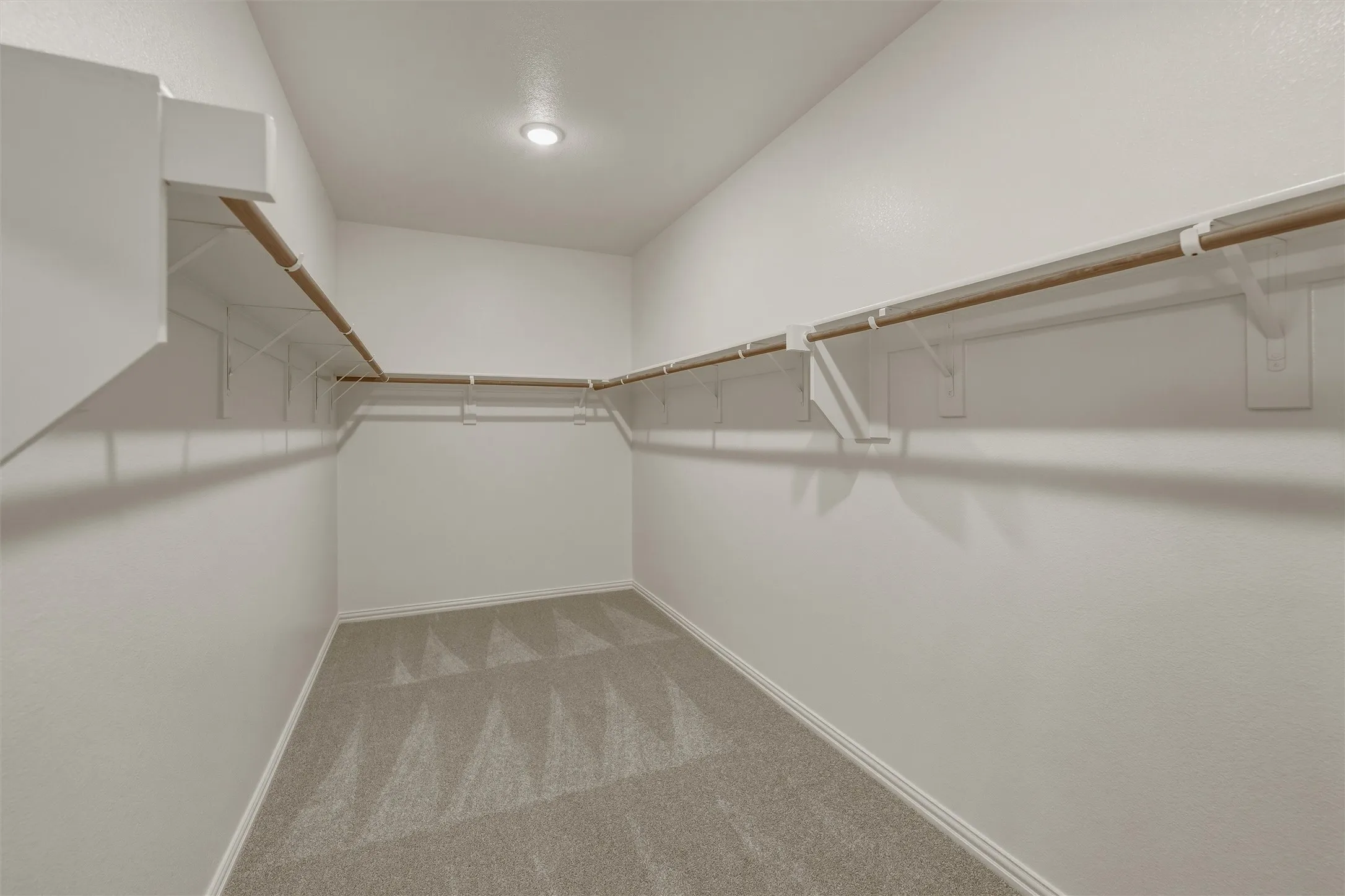 Walk-in closet featuring light gray patterned carpet, white baseboards, and built-in white shelving with natural wood rods
