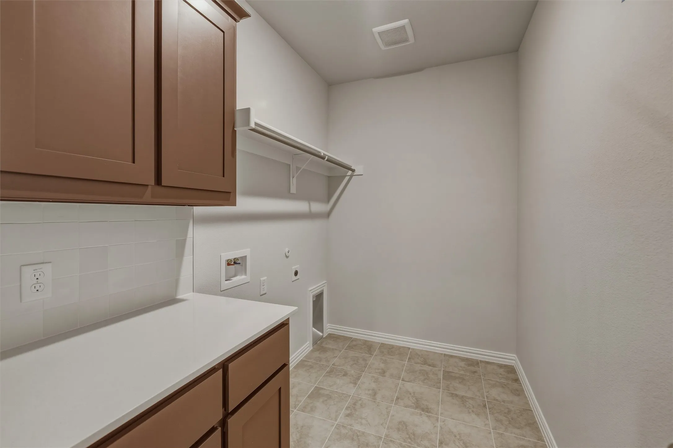 Laundry area featuring brown cabinetry, white countertop, white subway tile backsplash, and tile flooring