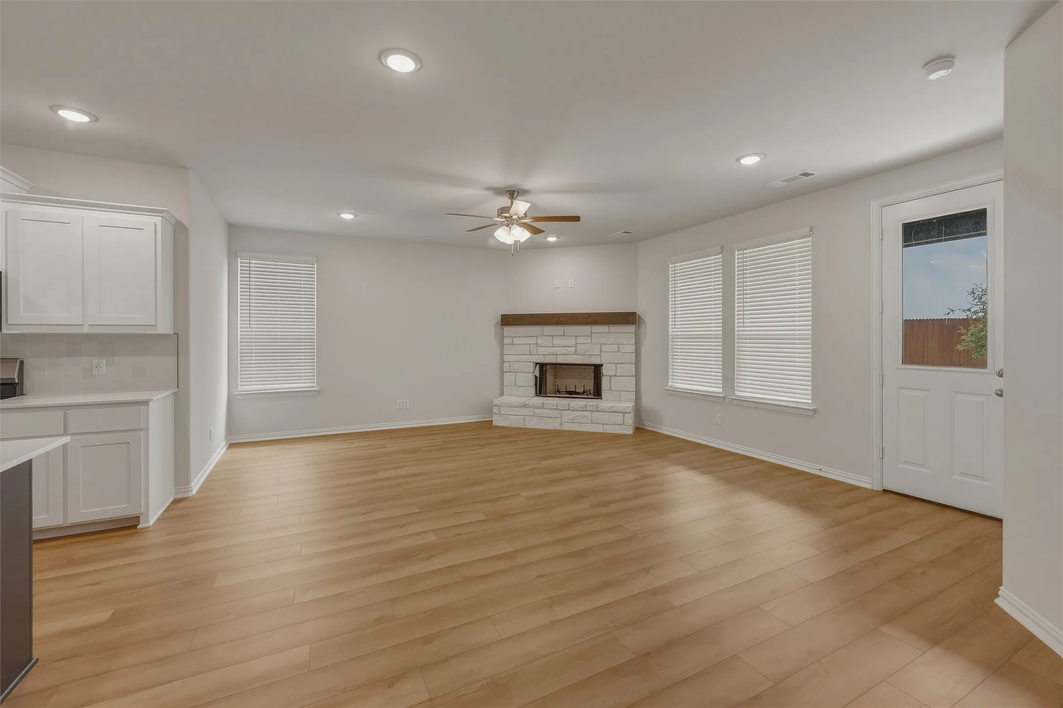 Open concept living space featuring wood-finish flooring, a white stone fireplace with a wood mantle, recessed lighting, and a ceiling fan