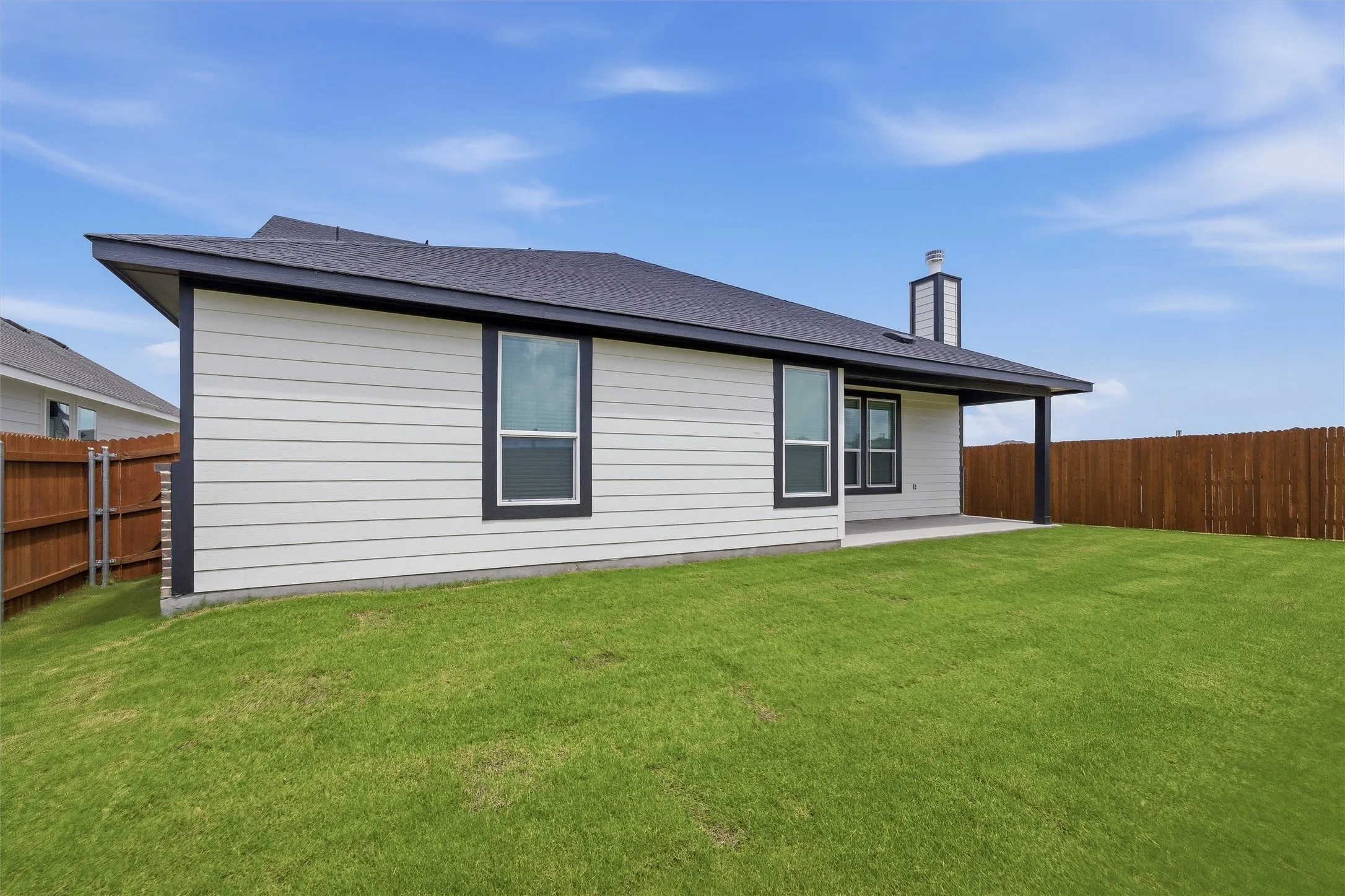 Spacious backyard featuring a covered patio, dark trim windows, horizontal siding, a substantial chimney, and wood fencing