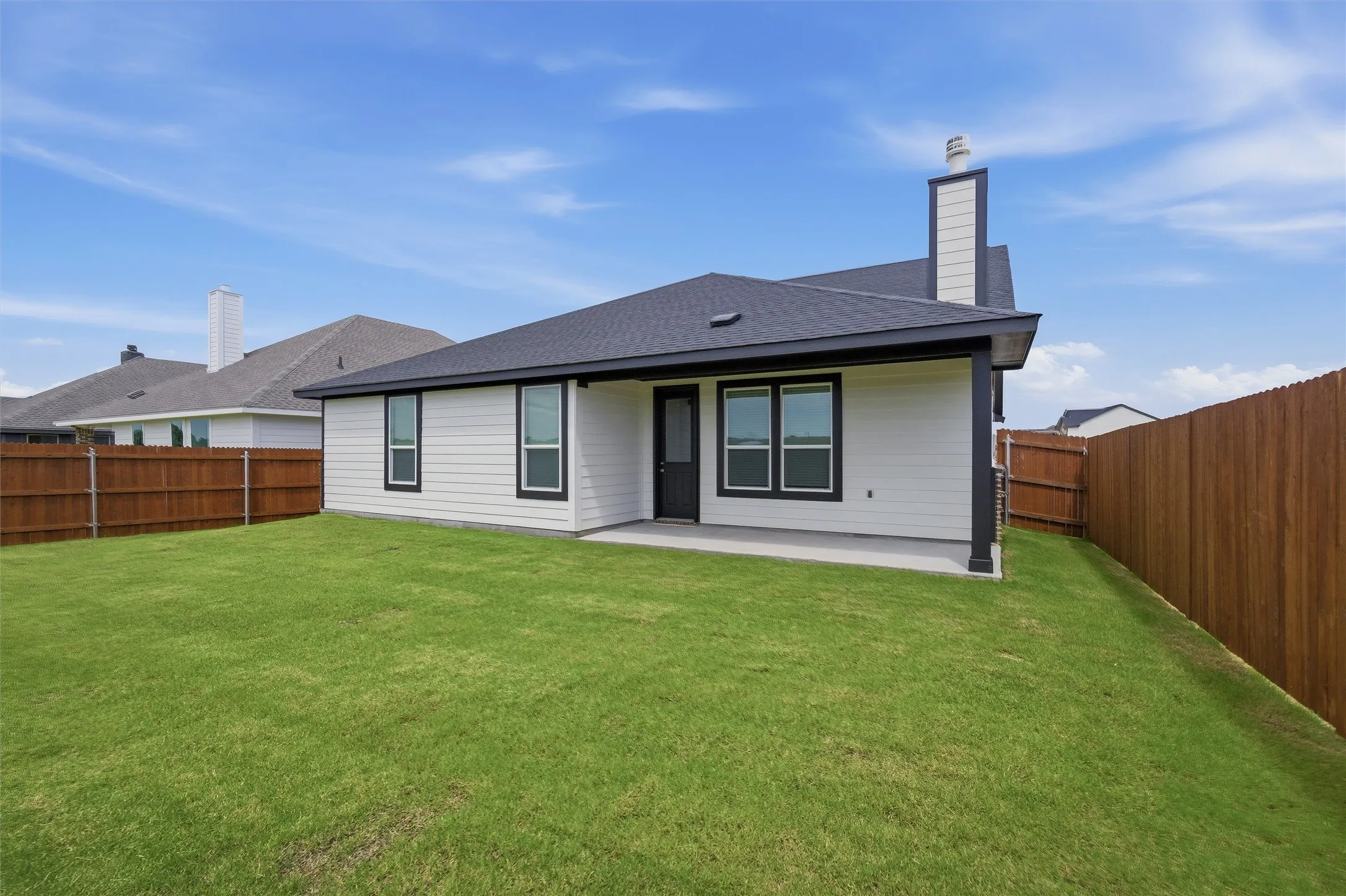 Spacious backyard with a substantial lawn area, featuring a covered patio, dark framed windows, and a privacy fence