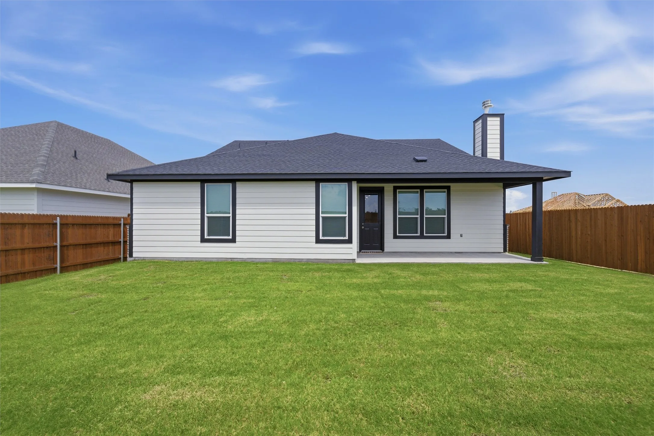 Expansive backyard featuring a covered patio, privacy fencing, and a white siding exterior with a dark roof