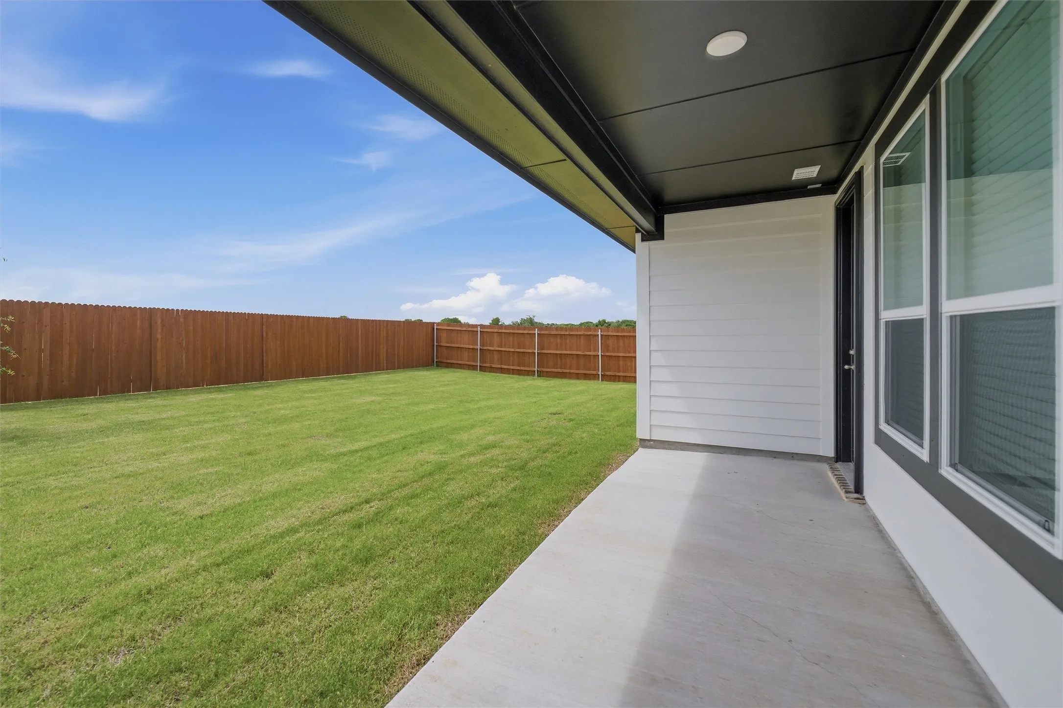 Expansive backyard featuring a lush lawn, solid wood privacy fencing, and a concrete patio