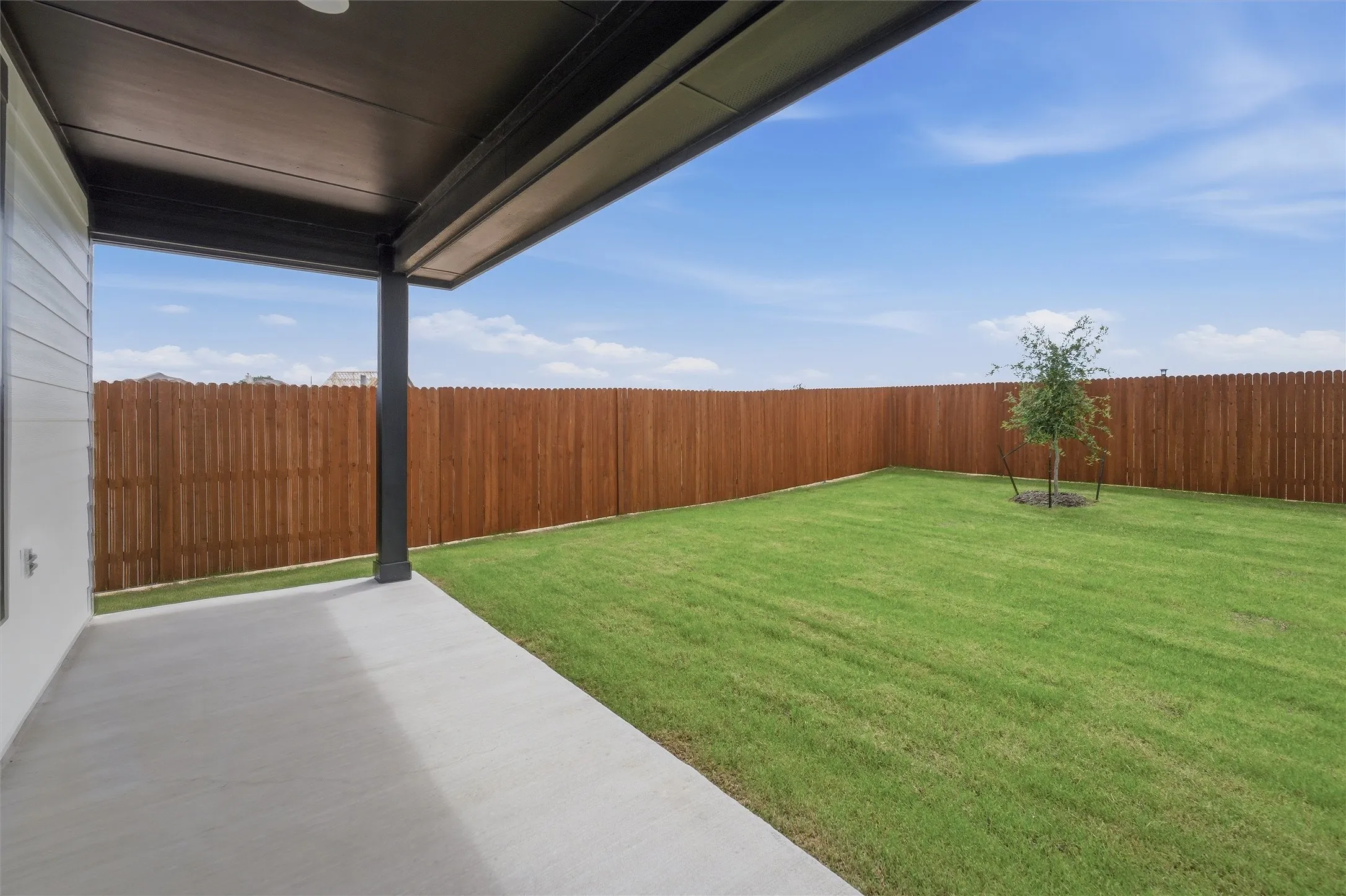 Expansive backyard featuring a manicured lawn, a young tree, and a full privacy fence
