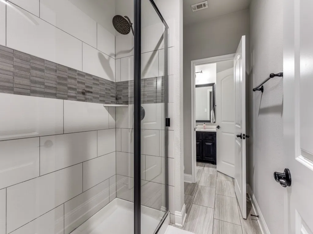 Walk-in shower featuring a rain showerhead, built-in shelving, and a glass enclosure with matte black trim