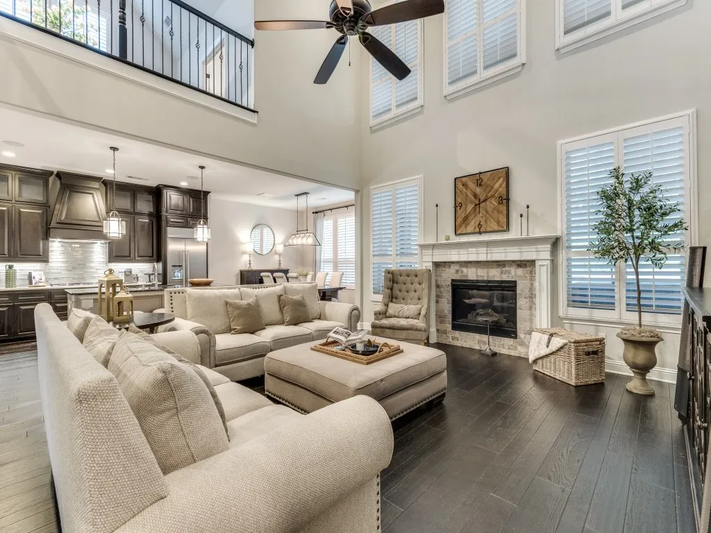 Two-story living area featuring dark wood-finish flooring, a fireplace with a stone surround and white mantel, and multiple windows with plantation shutters