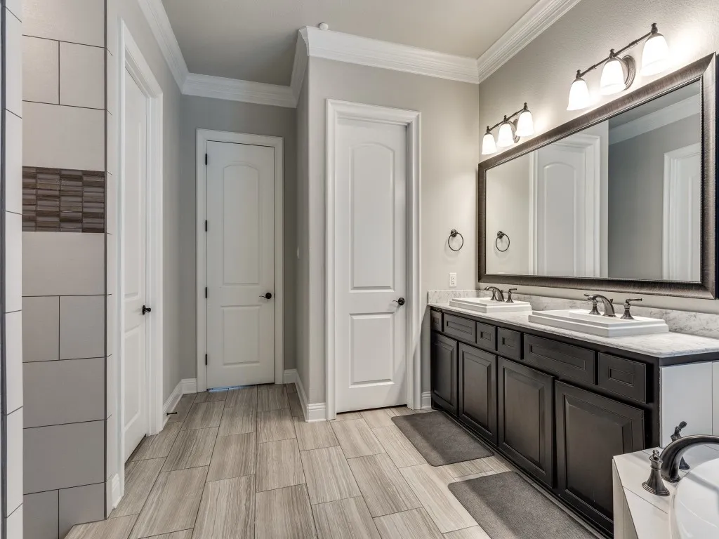 Bathroom featuring a double vanity with dark wood cabinetry, dual undermount sinks, and a single large framed mirror