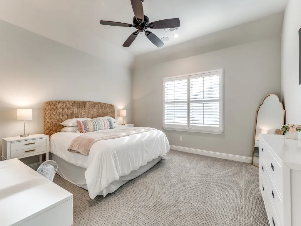 Bedroom featuring neutral wall paint, carpet flooring, a ceiling fan with integrated lighting, and a window with white louvered shutters
