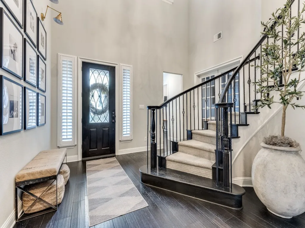 Inviting entryway featuring dark wood-finish flooring, a grand staircase with wrought iron balusters, and a custom front door with decorative glass