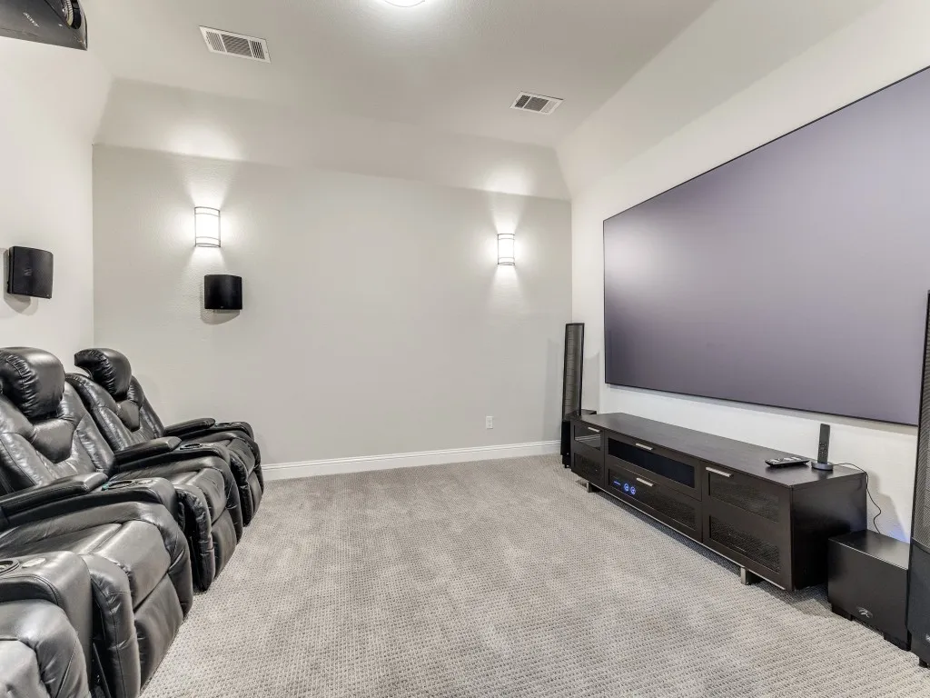 Dedicated media room featuring a large projection screen, recessed ceiling lighting, and wall-mounted sconces