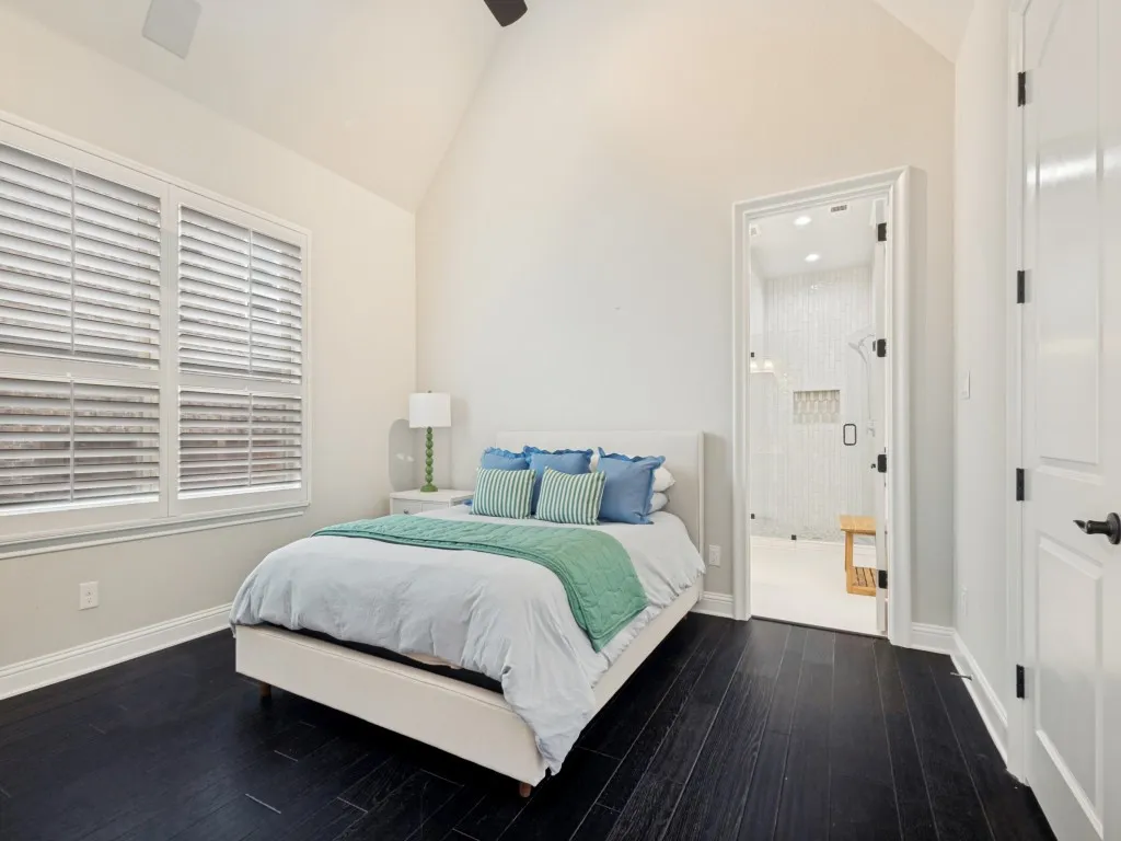 Bedroom featuring dark wood-finish flooring, a vaulted ceiling, and white plantation shutters