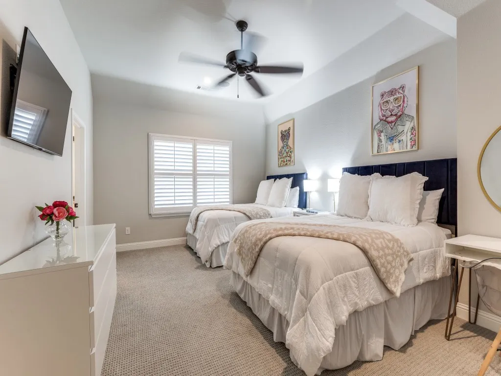Carpeted bedroom featuring two upholstered headboards, a ceiling fan, and window with plantation shutters