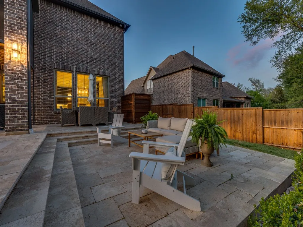 Spacious multi-level stone patio with integrated steps, featuring a full privacy fence, brick exterior, and outdoor wall sconce