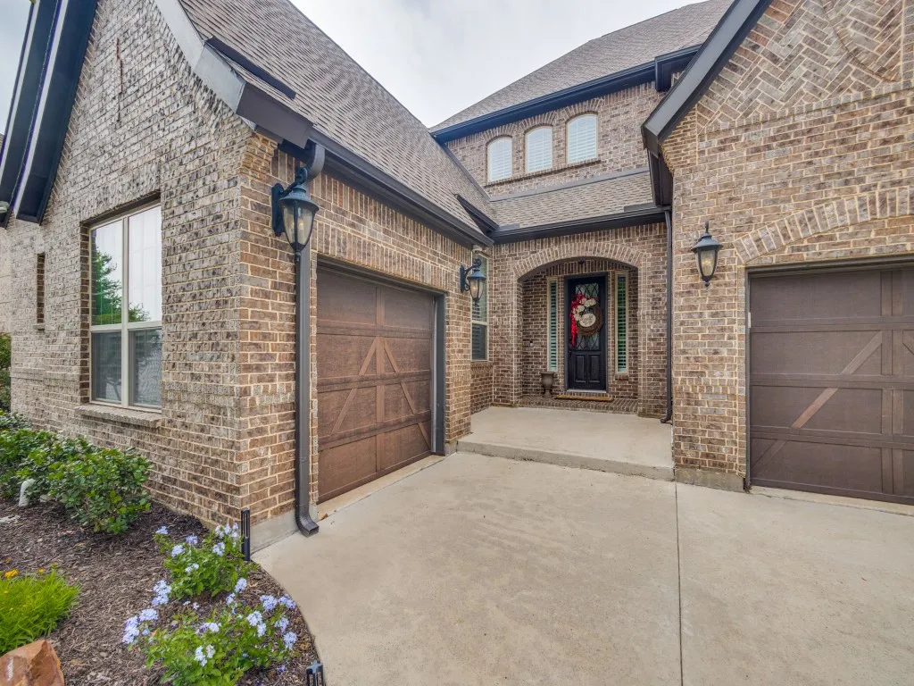 Brick exterior featuring an arched entry, dark wood garage doors, and decorative outdoor lighting fixtures