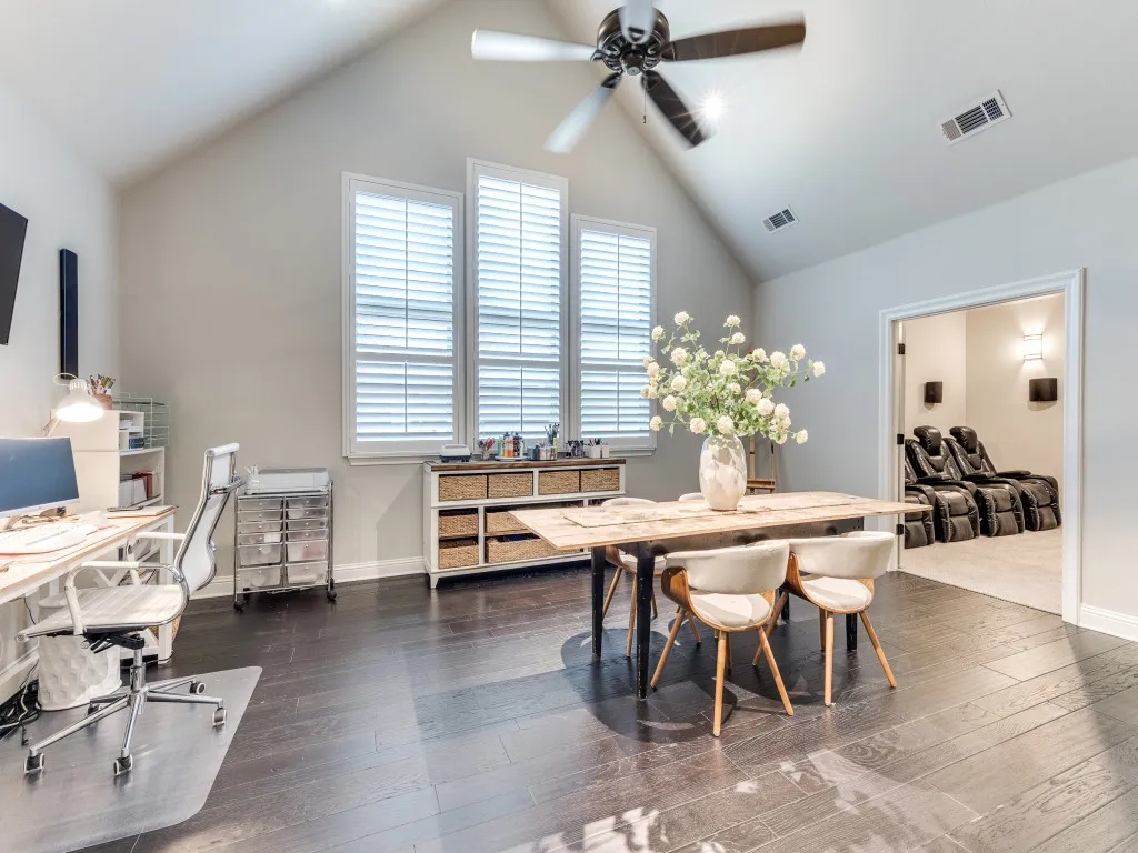 Vaulted ceiling room featuring dark wood-finish flooring, a ceiling fan, and multiple windows with plantation shutters