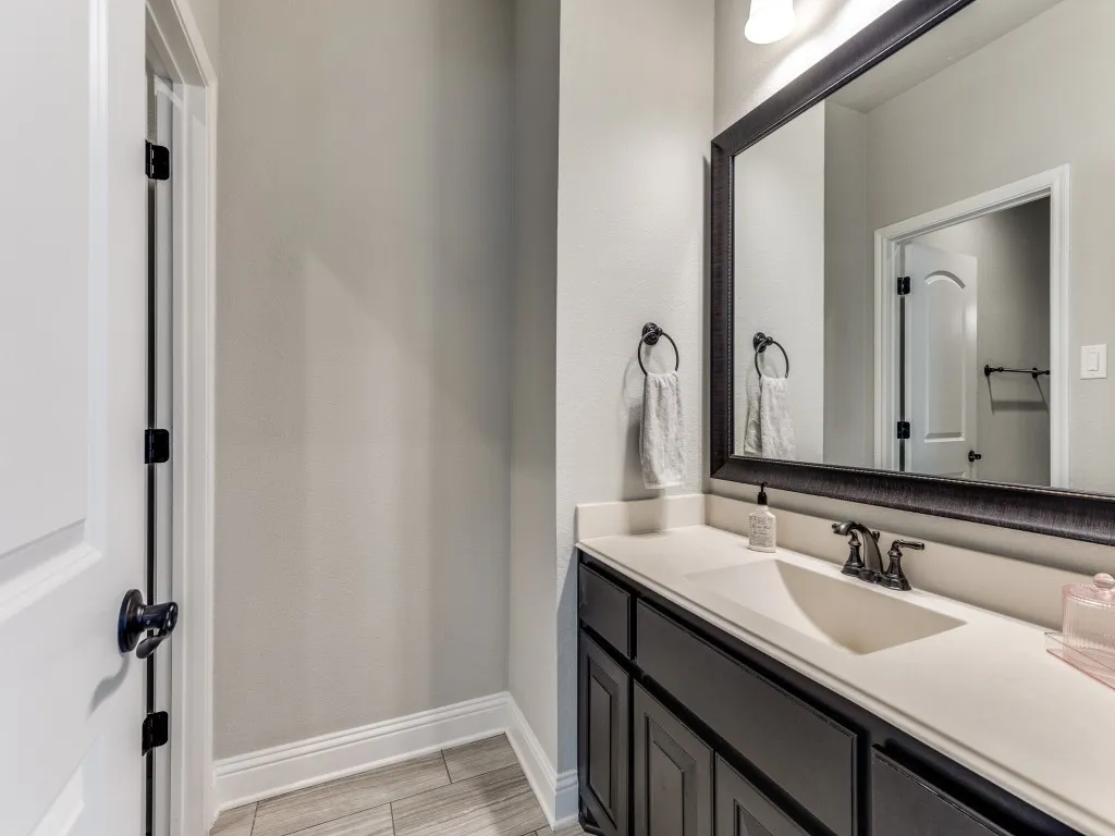 Bathroom vanity featuring a dark wood-finish cabinet, white countertop with integrated sink, and an ornate framed mirror