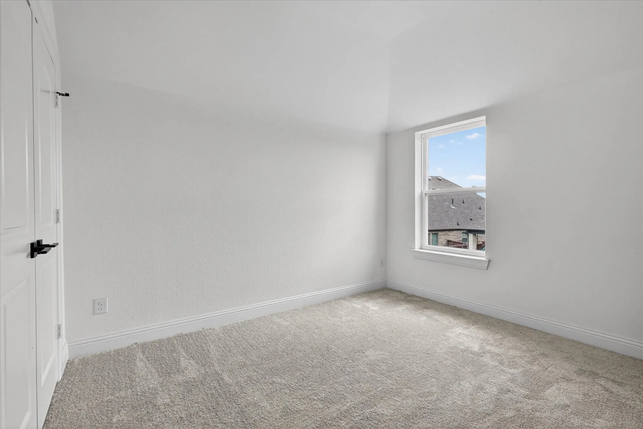 Bedroom featuring light gray carpeting, crisp white walls, a single window with white trim, and a white door with black hardware